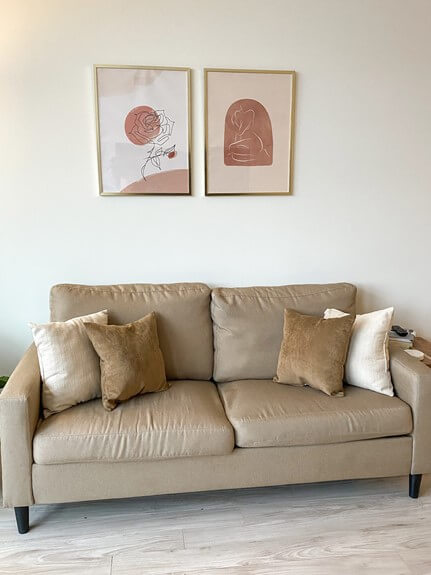 Tan couch with light brown and white throw pillows. unique wall deco with gold frames